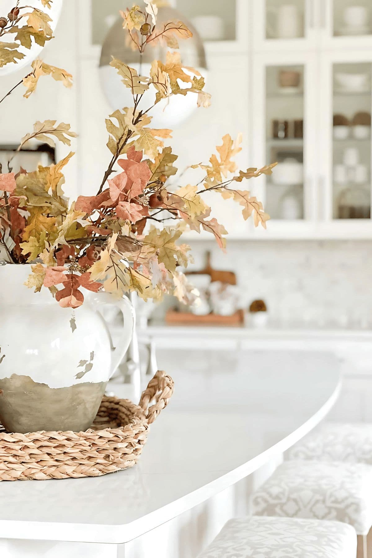 Autumn leaf arrangement in a white pitcher on a farmhouse-style table.