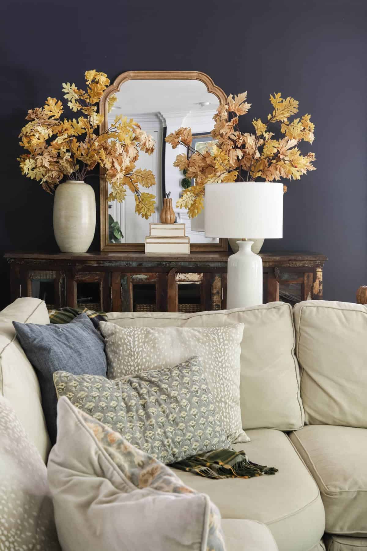Vase with dried autumn leaves and a mirror on a dark wall in a cozy living room.