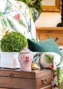 Vase with green plant, decorative ginger jar, and colorful floral bedding on a wooden nightstand.