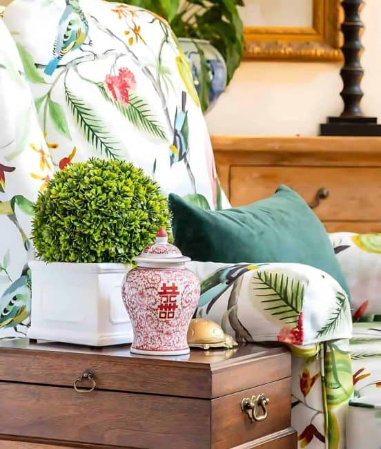 Vase with green plant, decorative ginger jar, and colorful floral bedding on a wooden nightstand.