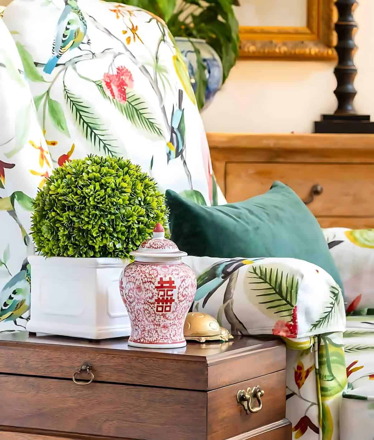 Vase with green plant, decorative ginger jar, and colorful floral bedding on a wooden nightstand.
