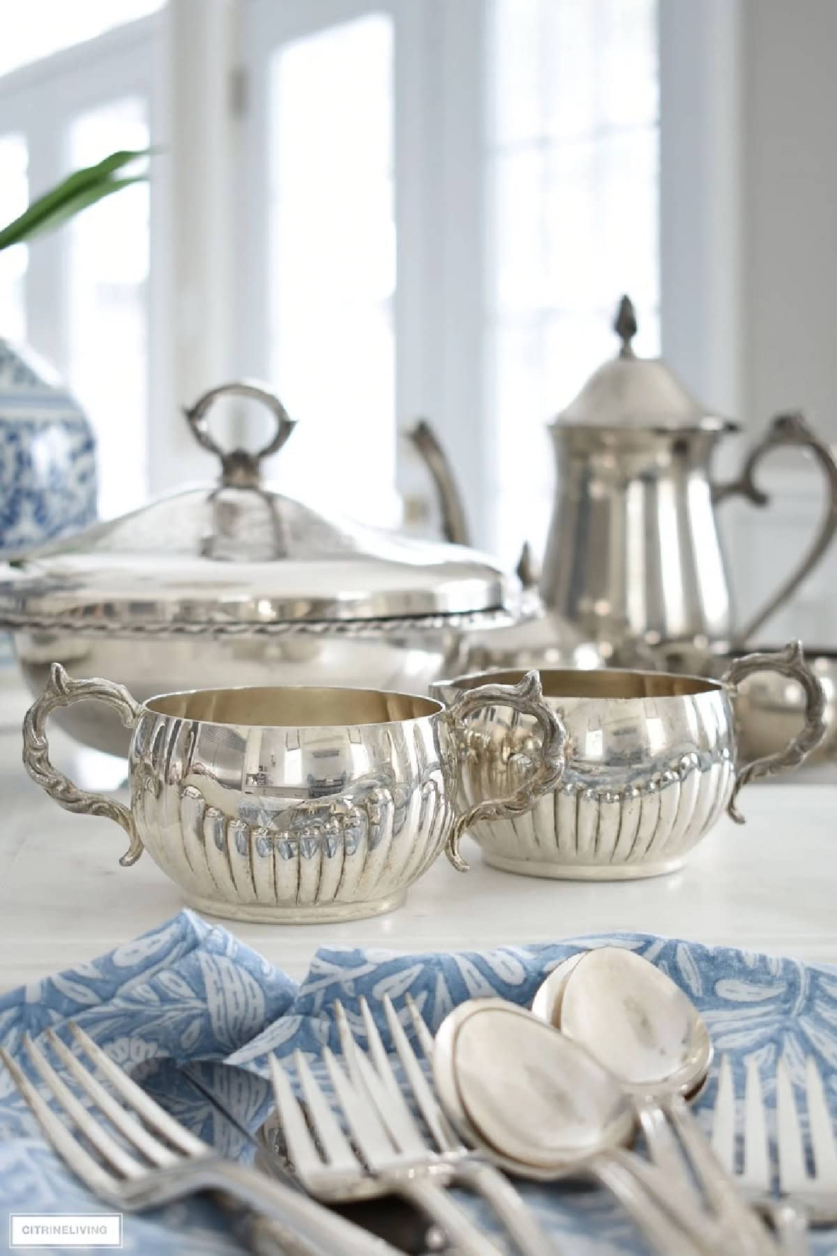 Silver vintage tea set with ornate handles on a white table with blue patterned napkin and cutlery, styled for DIY home decor.