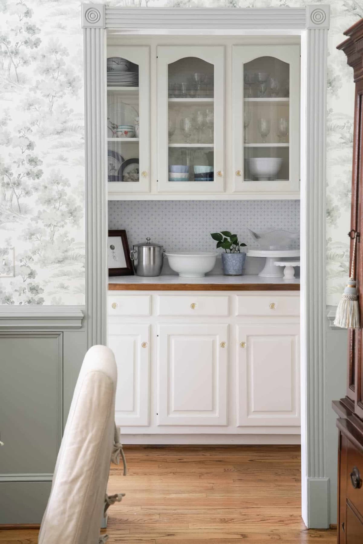 Vintage white kitchen cabinet with glass doors displaying dishes and glassware.