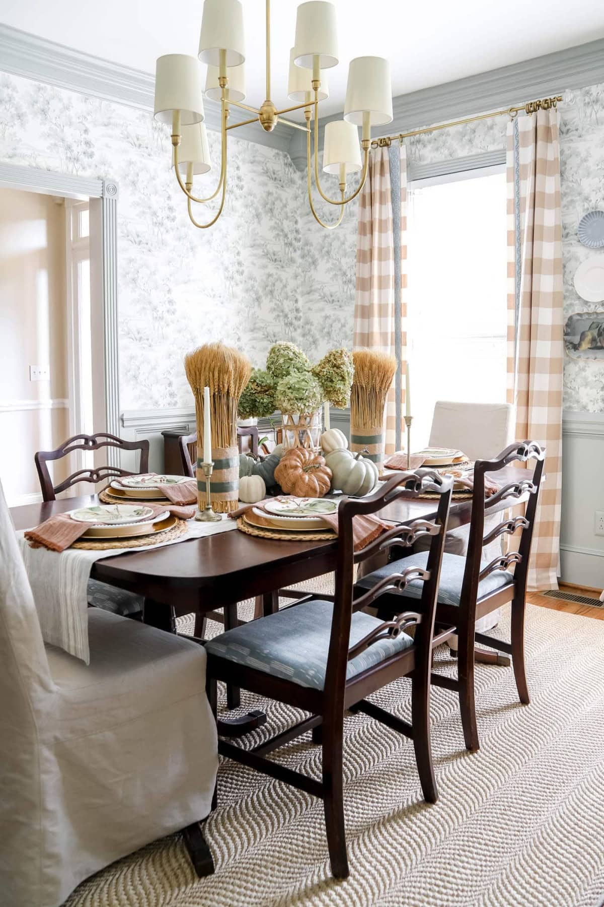 Vintage wooden dining table with fall-inspired decor including pumpkins and dried flowers.