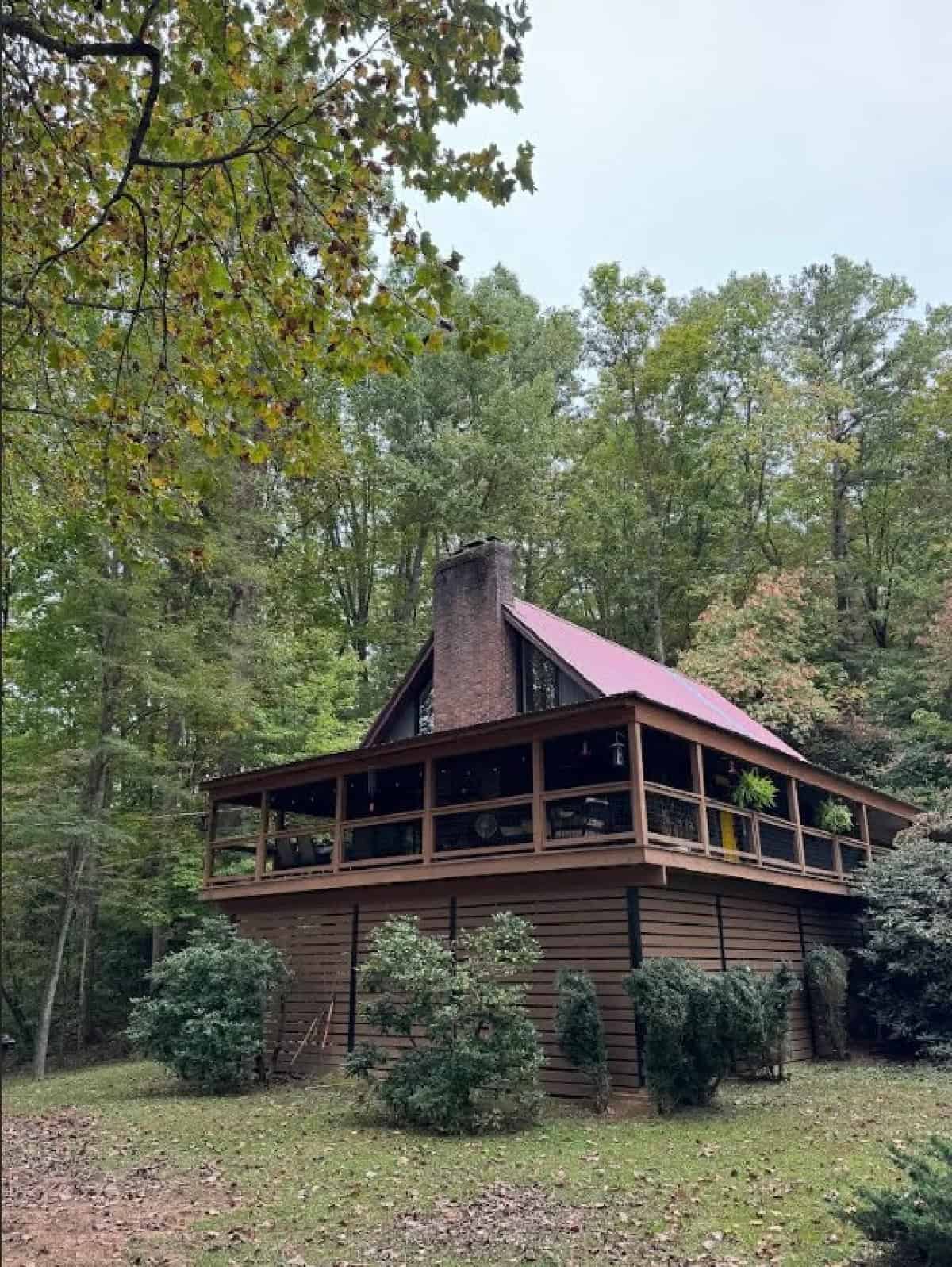 Wooden A-frame cabin surrounded by lush trees in a forest setting.