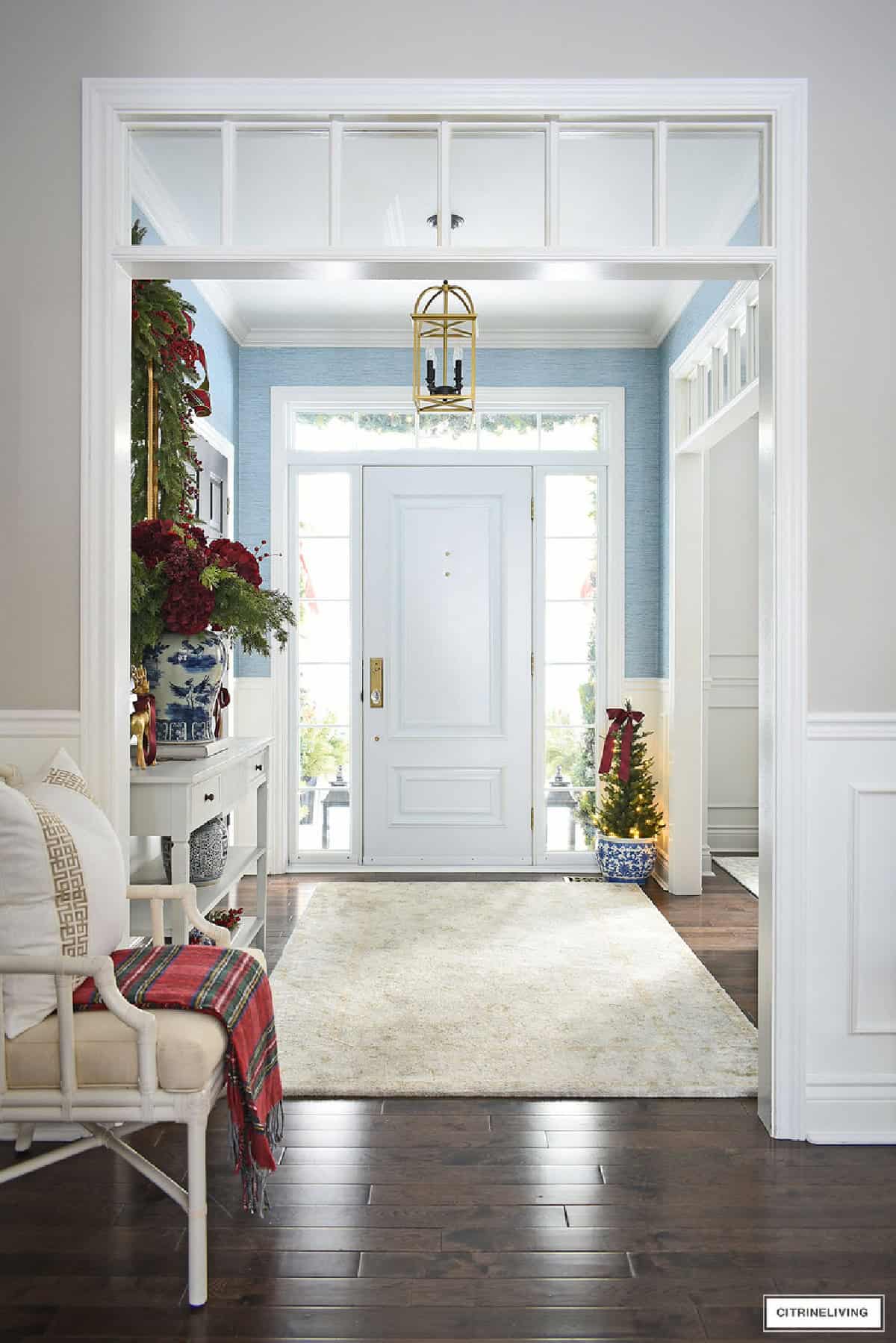 White front door with glass panes and blue wall, entryway decorated for Christmas.
