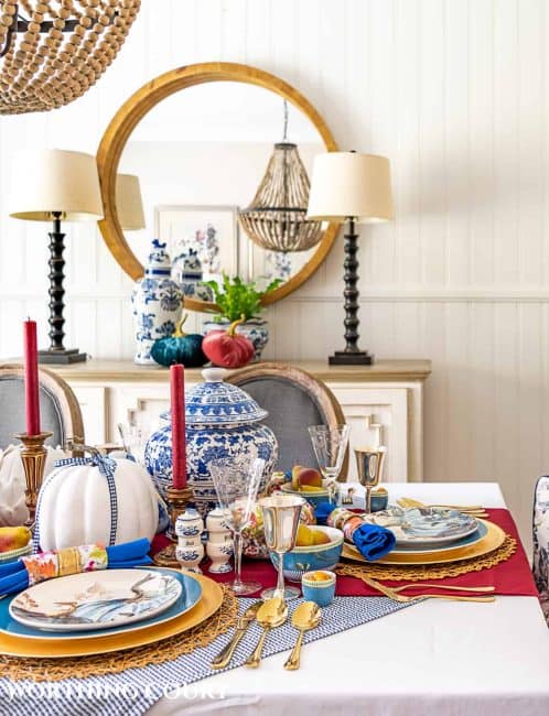 Colorful farmhouse dining table with elegant tableware and pumpkins for fall decor.