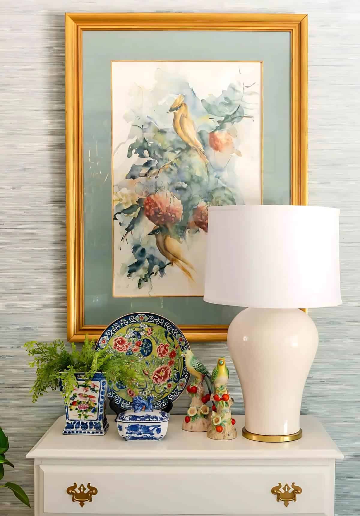frame art hanging above a small white chest with chinoiserie accessories