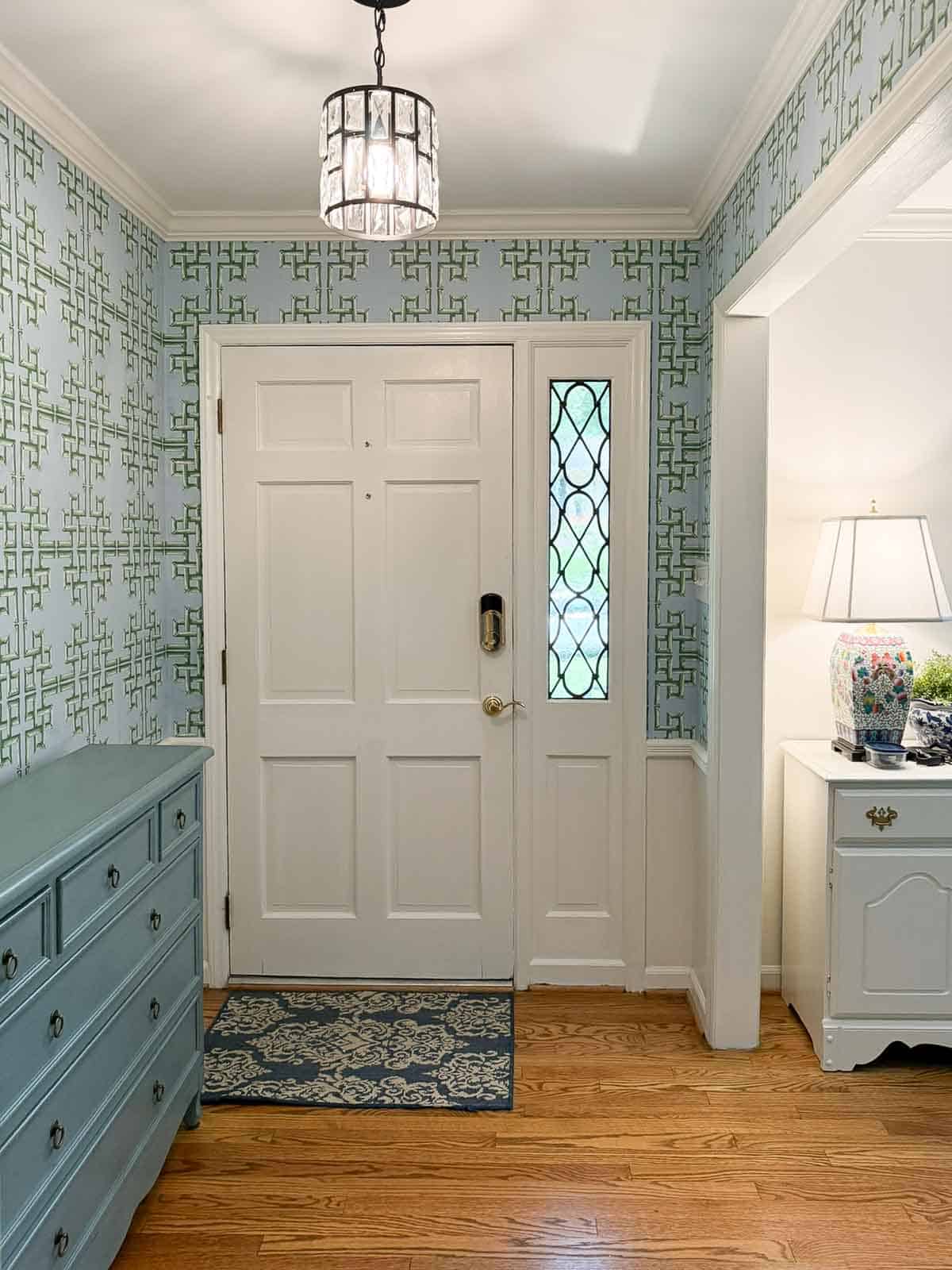 views of a small foyer decorated with chinoiserie accessories, a wood console table, and with blue and green lattice patterned wallpaper