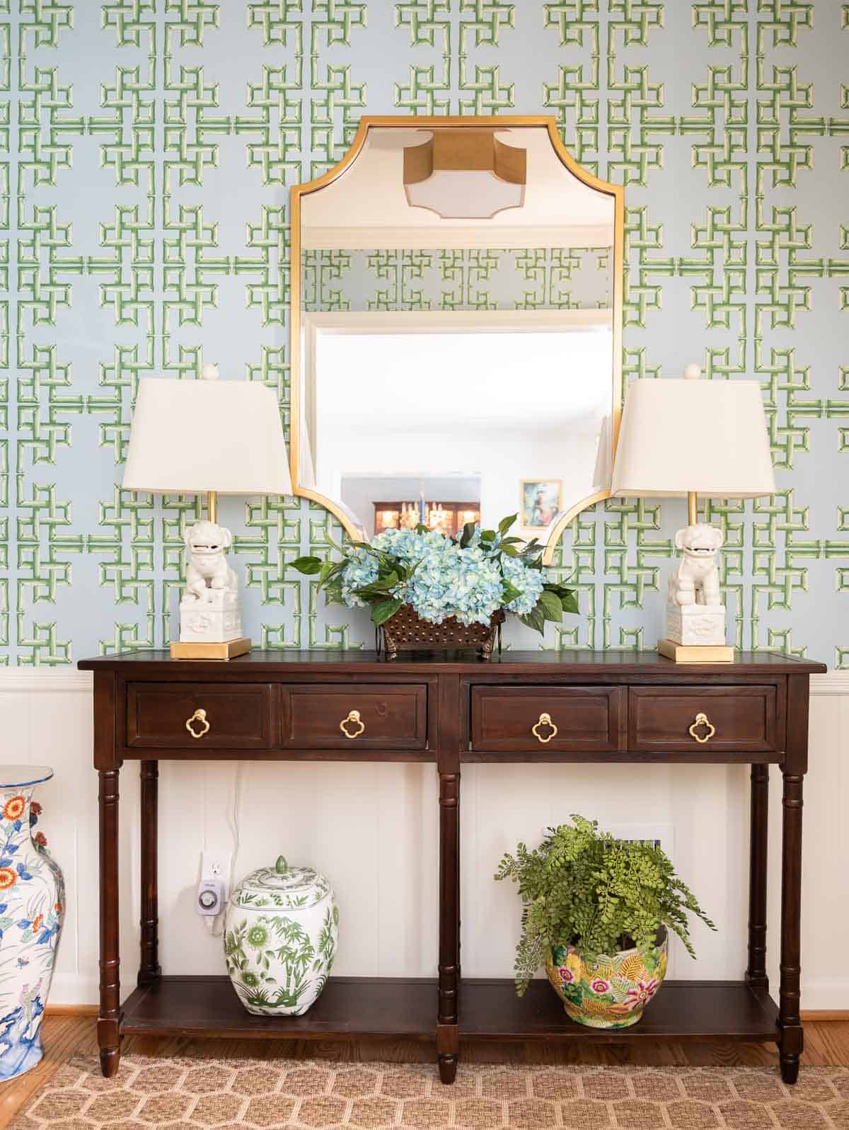 views of a small foyer decorated with chinoiserie accessories, a wood console table, and with blue and green lattice patterned wallpaper