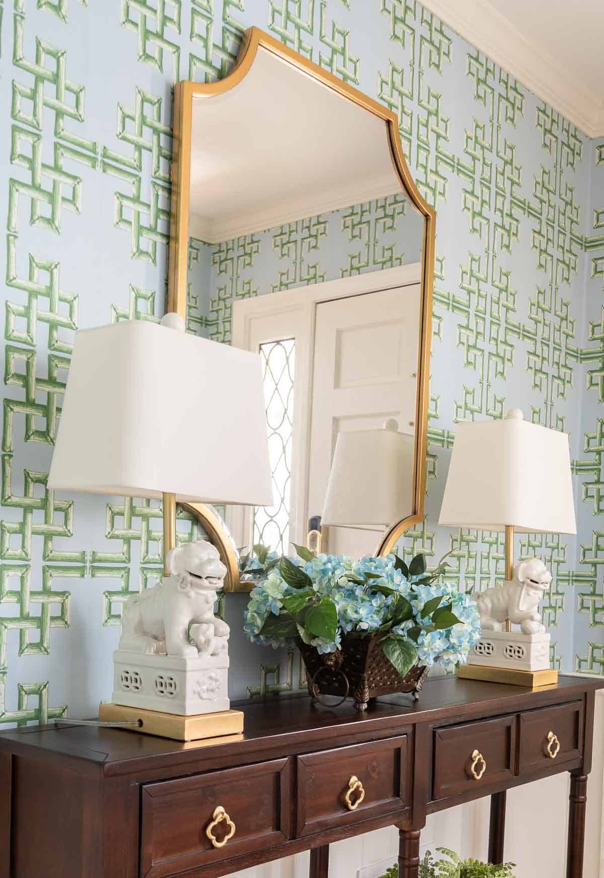 views of a small foyer decorated with chinoiserie accessories, a wood console table, and with blue and green lattice patterned wallpaper