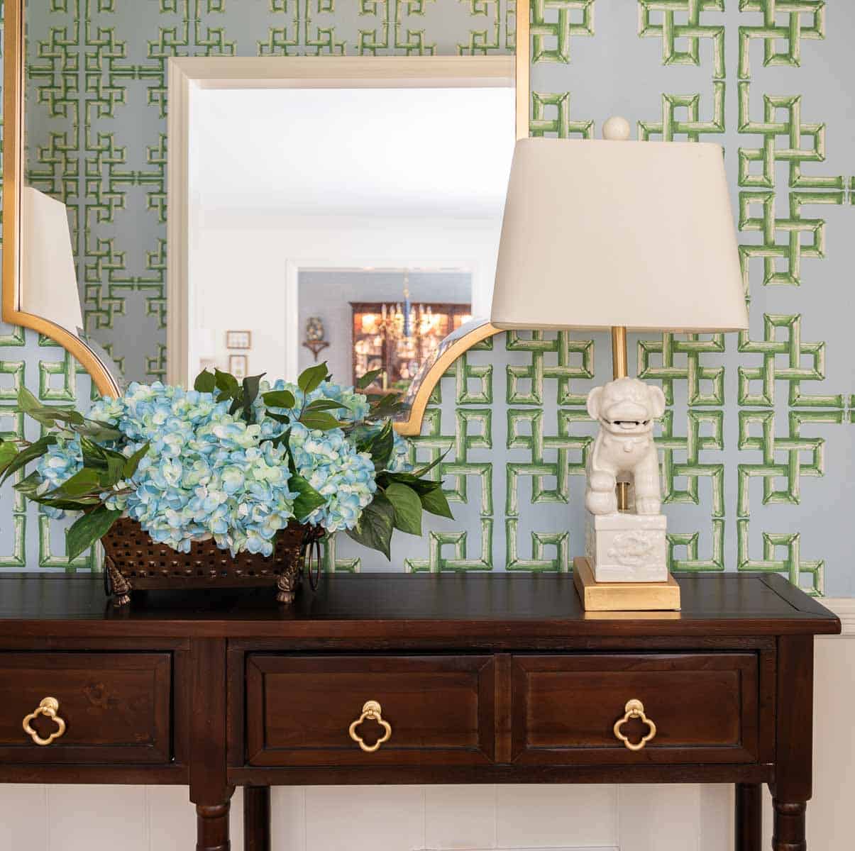 views of a small foyer decorated with chinoiserie accessories, a wood console table, and with blue and green lattice patterned wallpaper