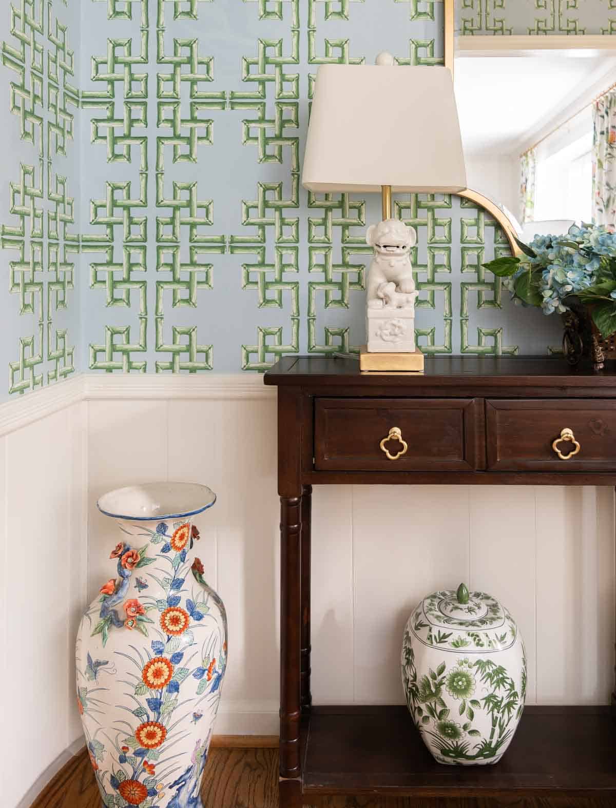 views of a small foyer decorated with chinoiserie accessories, a wood console table, and with blue and green lattice patterned wallpaper