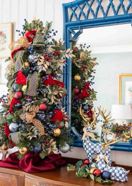 Decorated Christmas tree with blue, red, gold ornaments and ribbons in a holiday home setting.