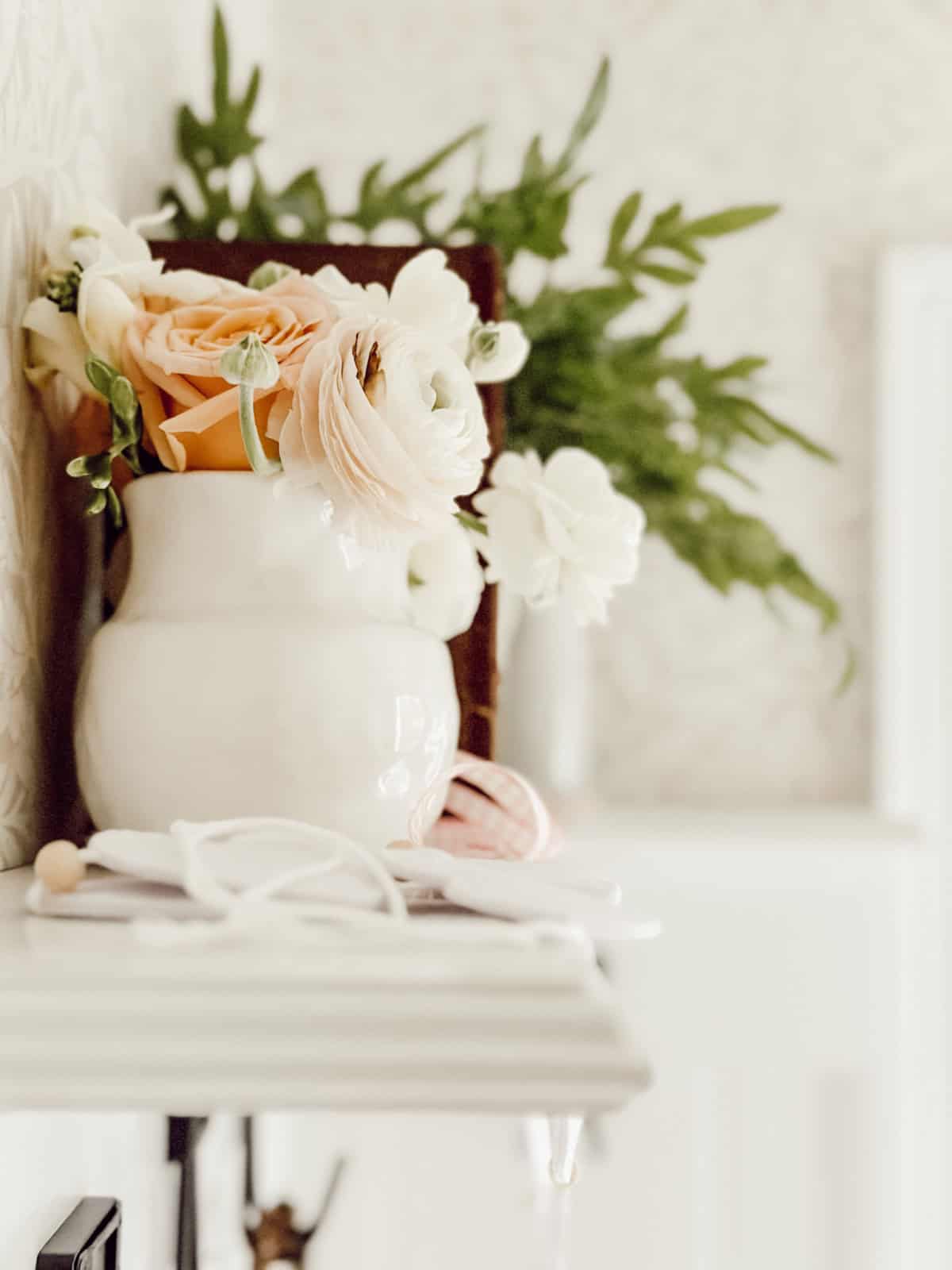 pale pink flowers arranged in a white vase on a white mantel