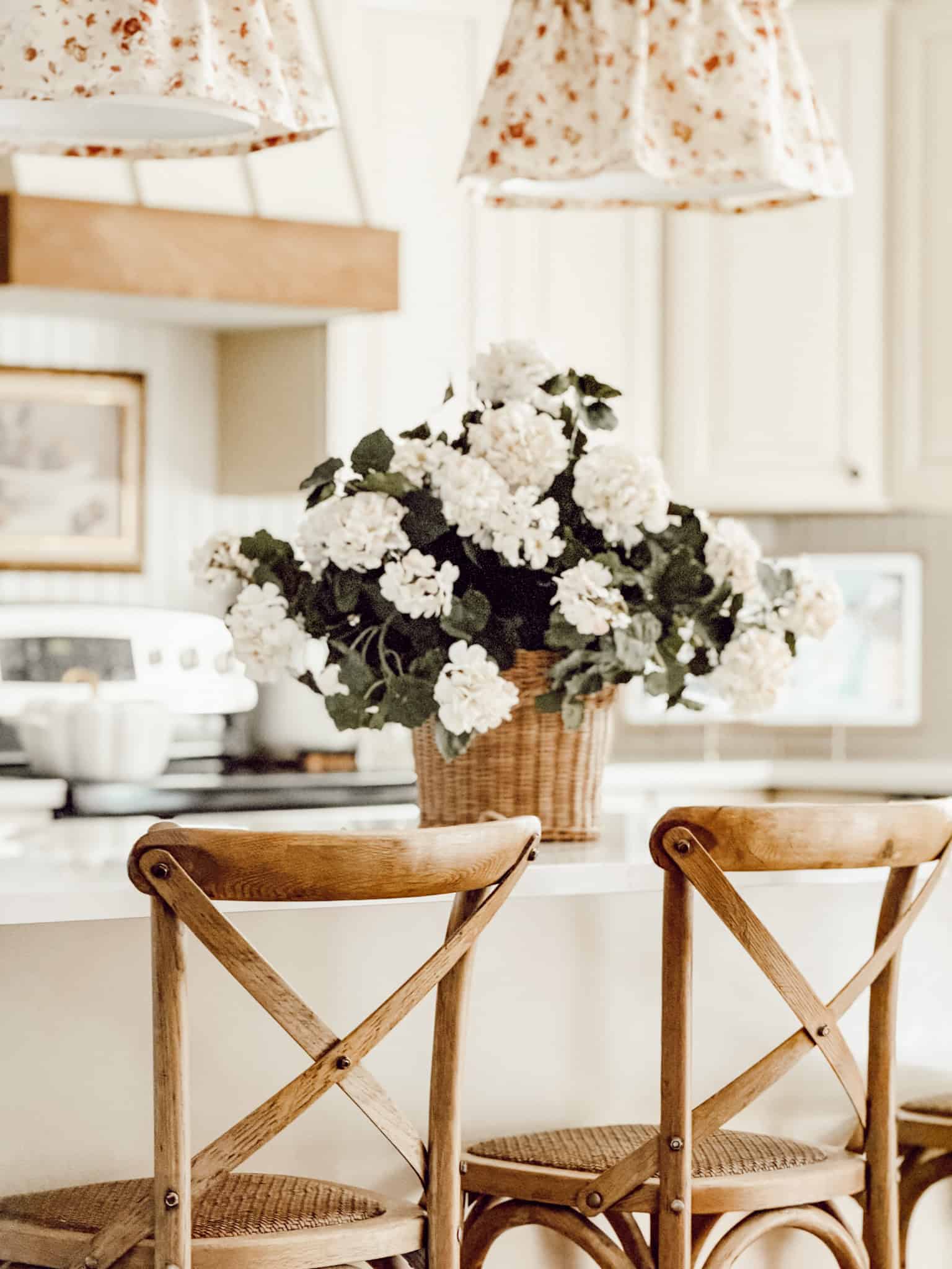 wicker basket filled with white hydrangeas on a kitchen island with cross-back wood bar stools in the foreground