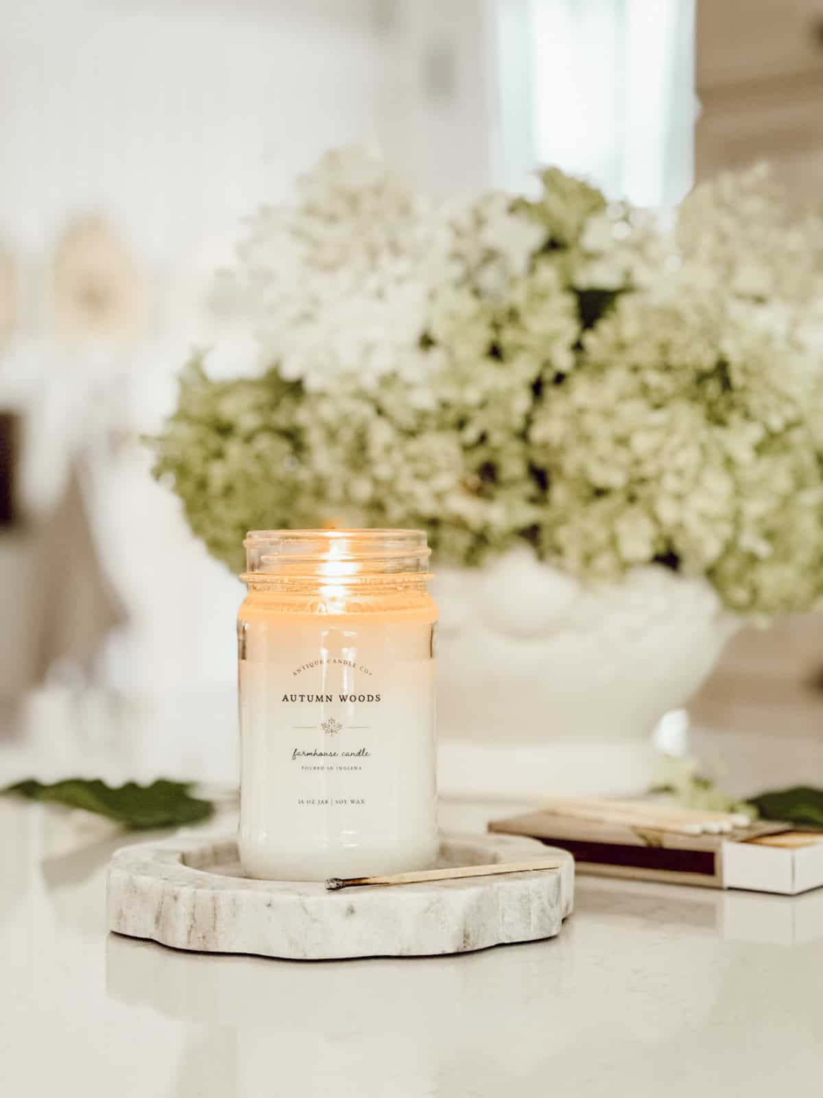 burning candle in a mason jar on a marble coaster in front of a hydrangea arrangement