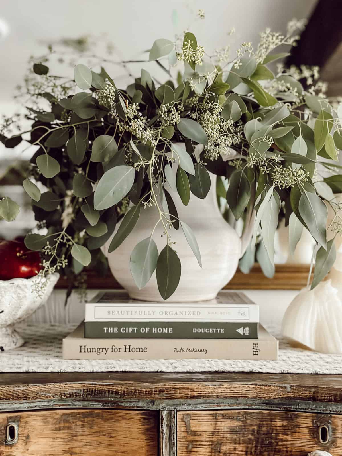 white urn filled with real berried eucalyptus leaves on a stack of coffee table books