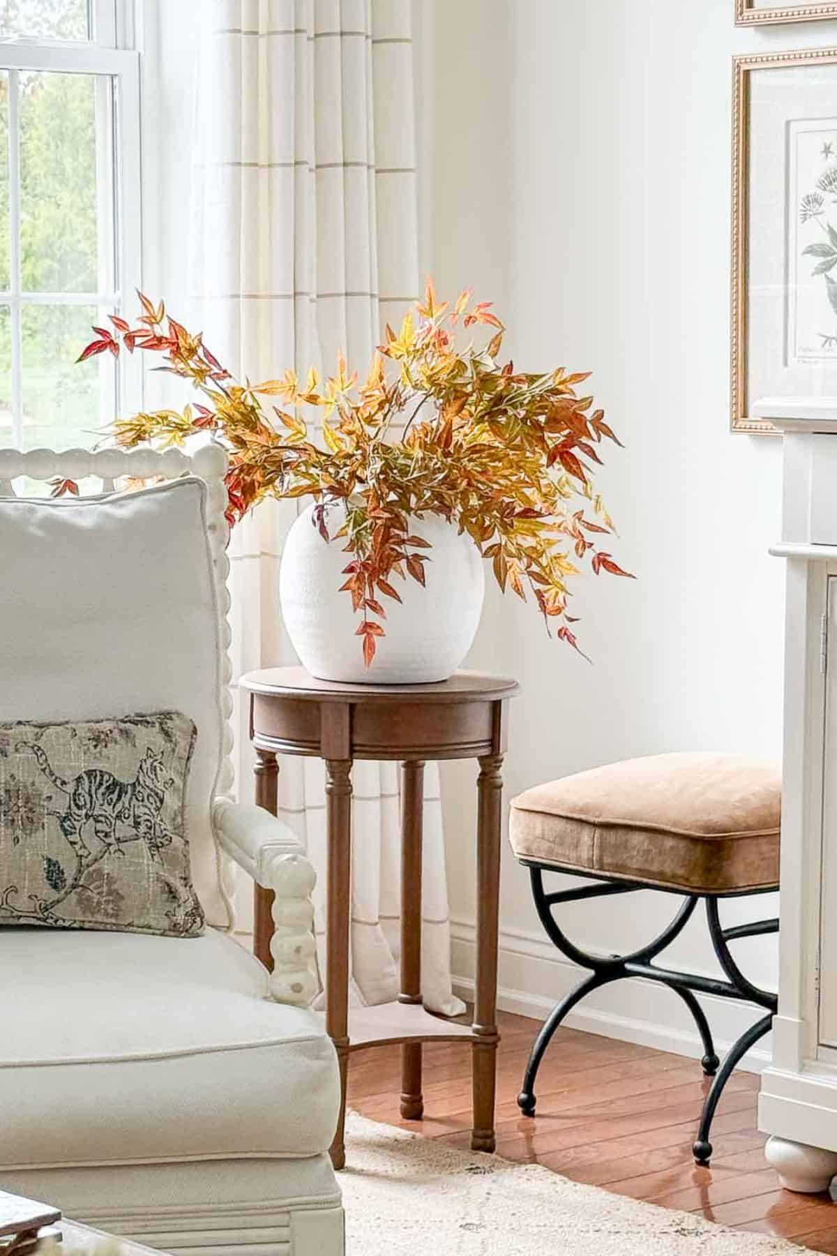 fall foliage stems in a white vase on a round wooden pedestal