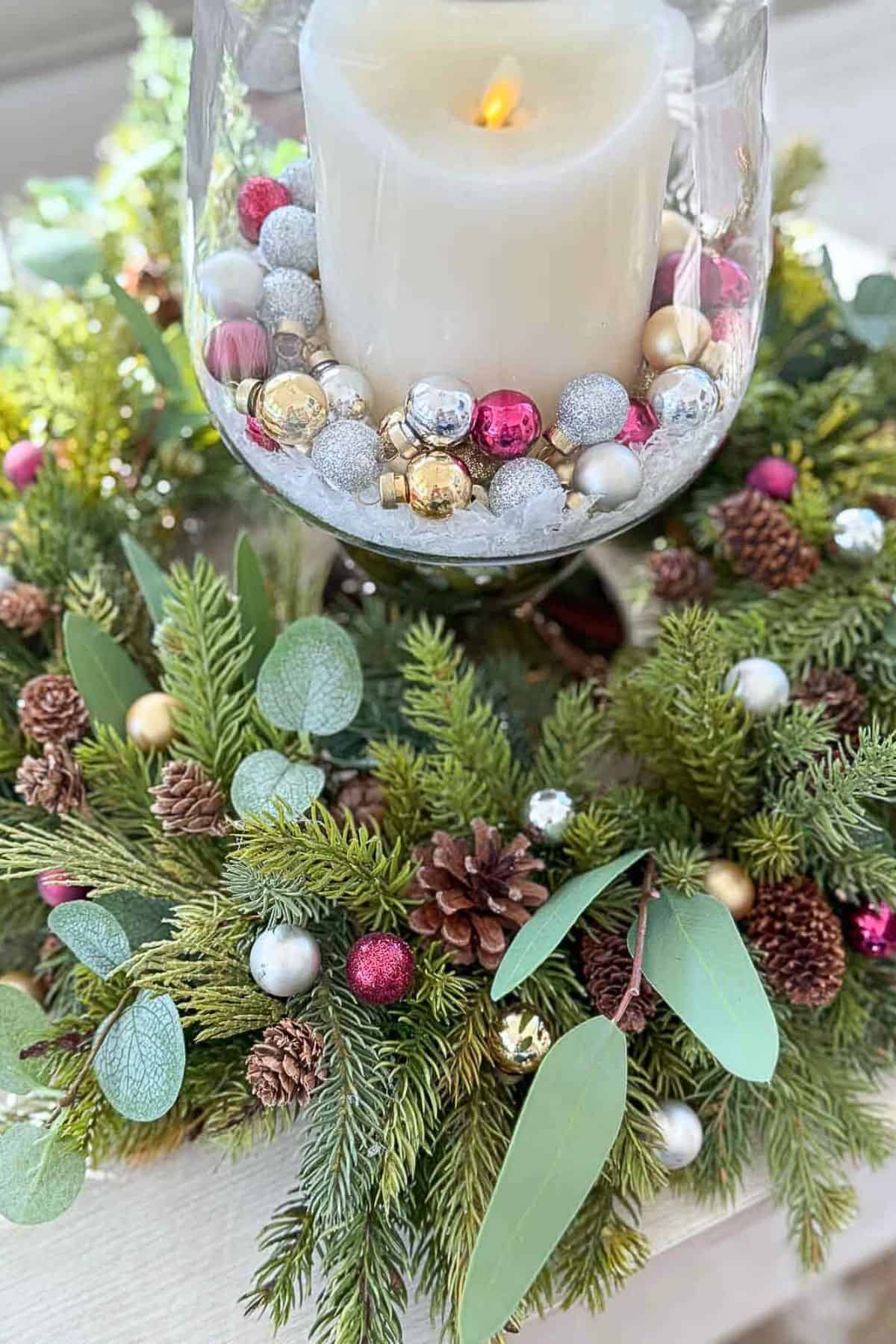 white candle in a glass hurricane surrounded by Christmas greenery