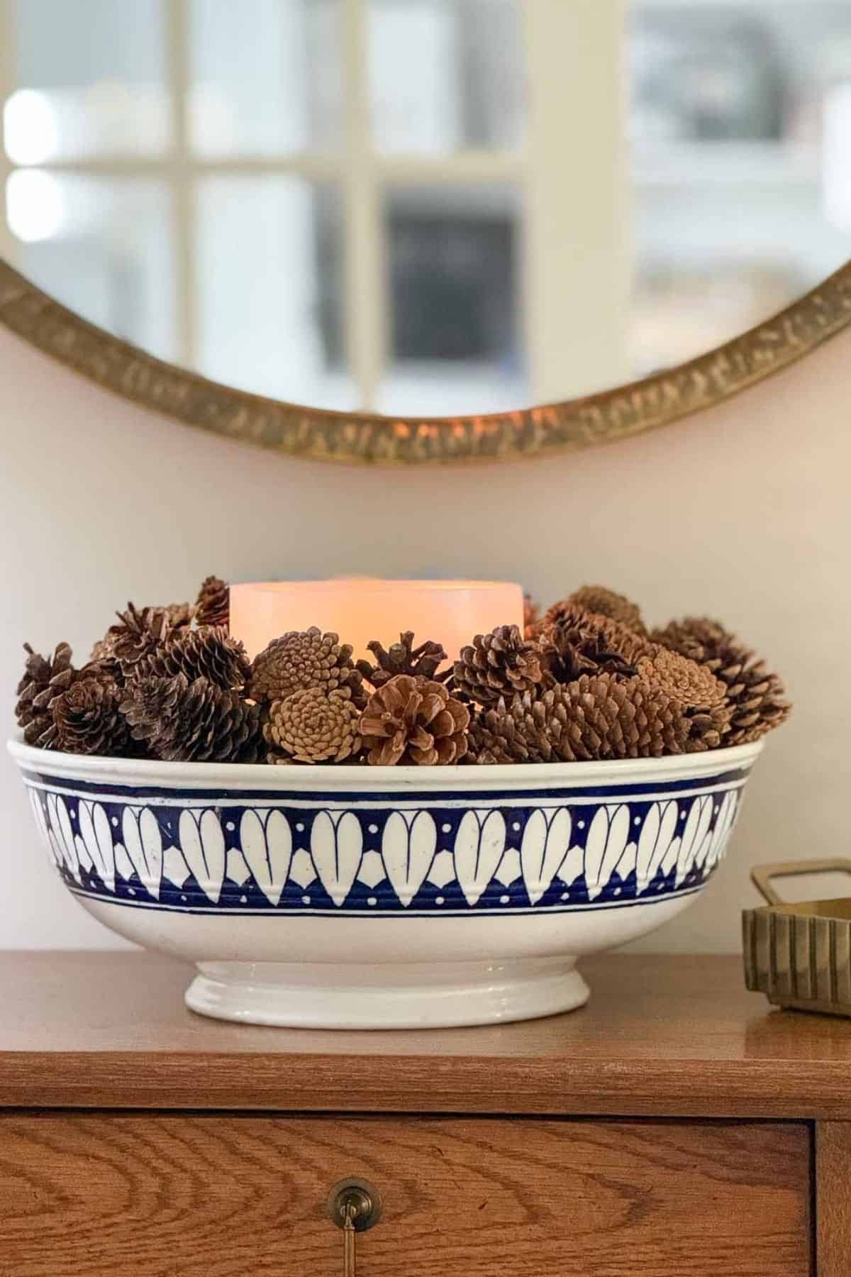 blue and white bowl filled with pine cones and a candle