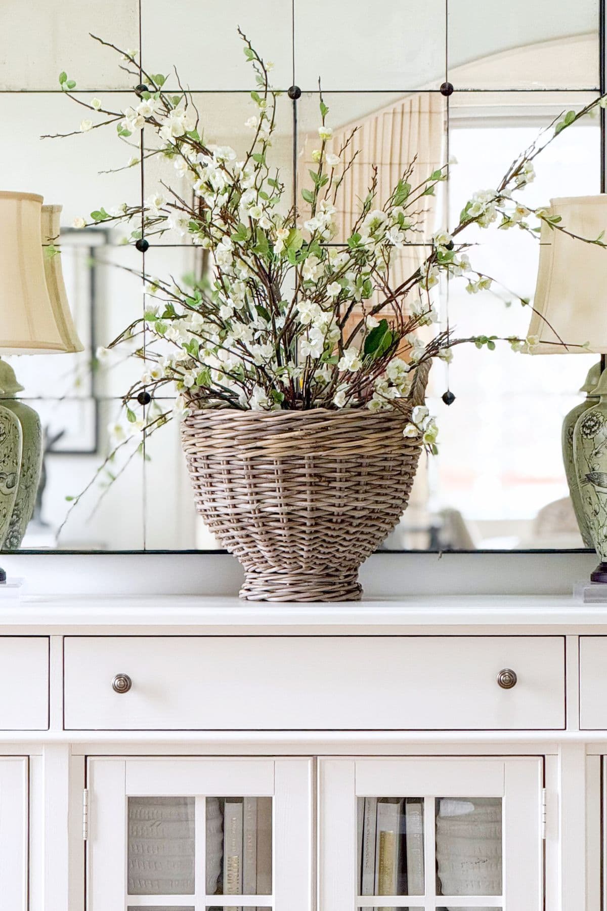 wicker container filled with white floral stems on a console in front of a large mirror