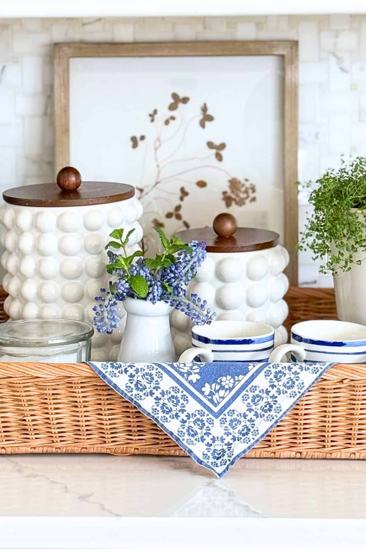white canisters in a wicker tray mixed with other blue and white accessories on a kitchen counter