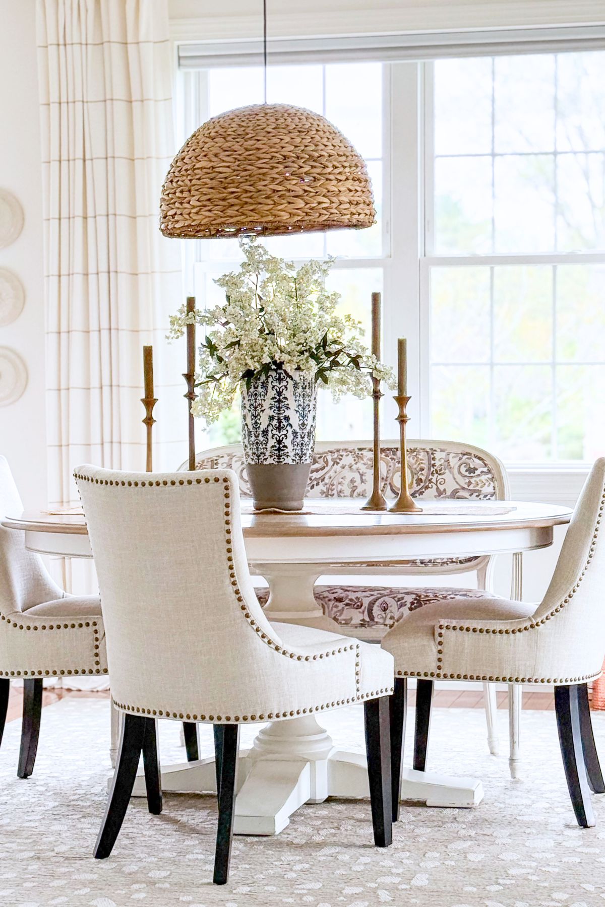 round dining table surrounded with chairs upholstered in neutral fabric with a floral centerpiece in a blue and white vase