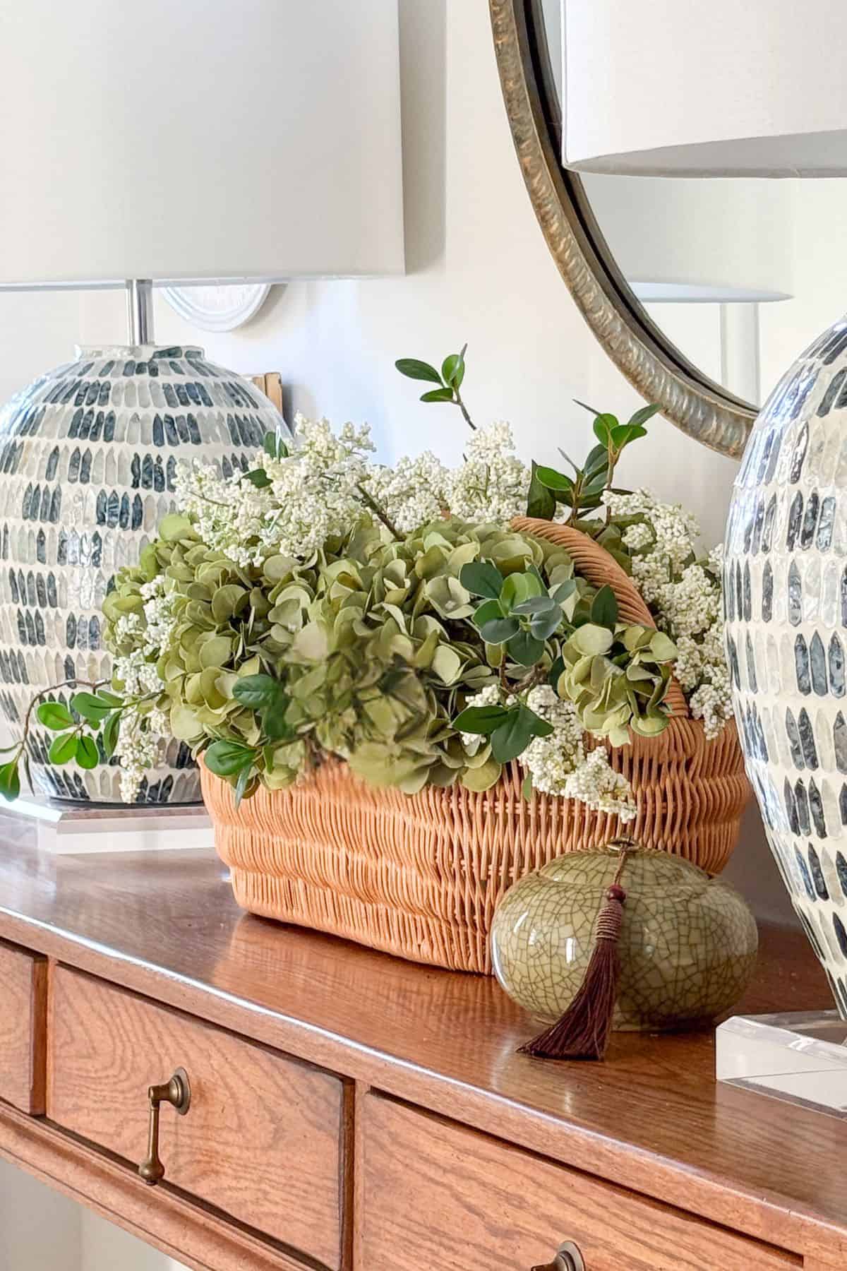 artificial greenery in a basket between two table lamps