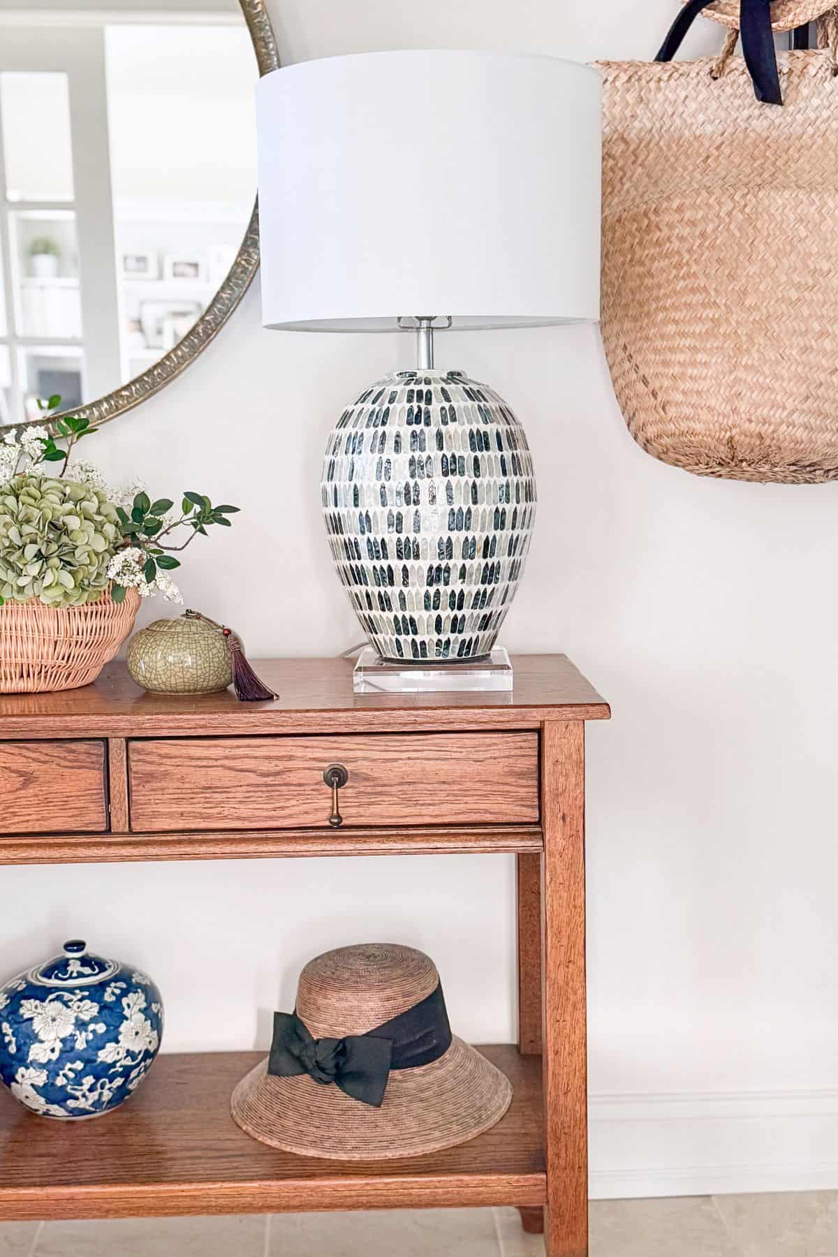 lamp with black and white base on a wood console table below a round mirror