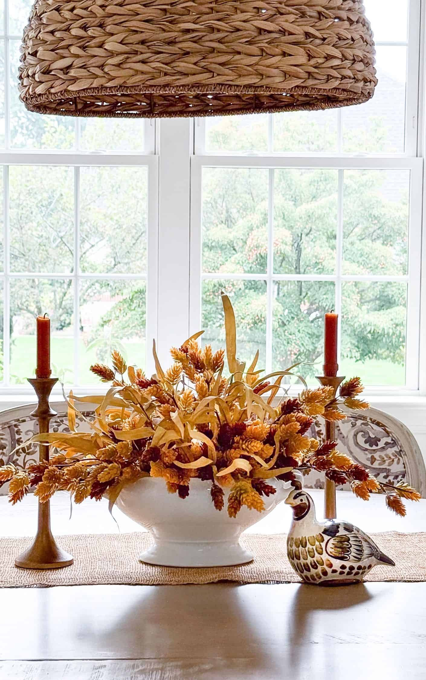 fall centerpiece flanked with fall candles and a small quail figurine on a wood tabletop