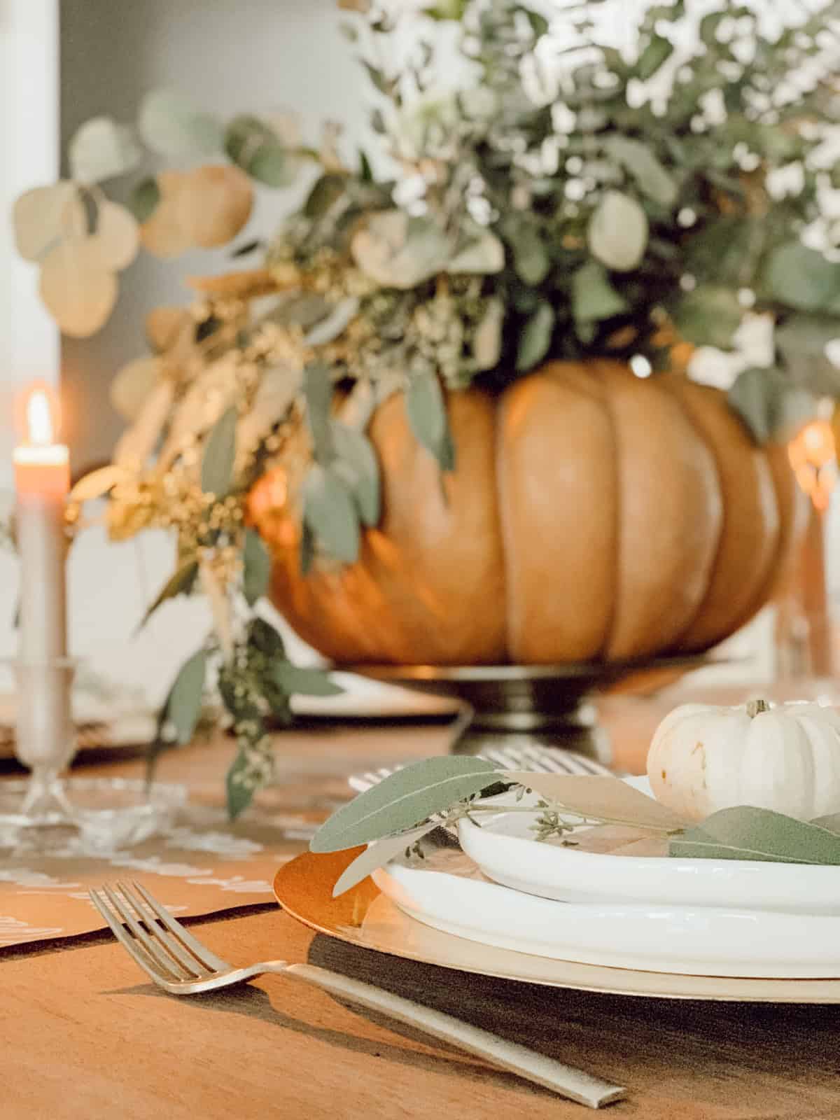 large faux pumpkin filled with dried eucalyptus stems on a fall table setting