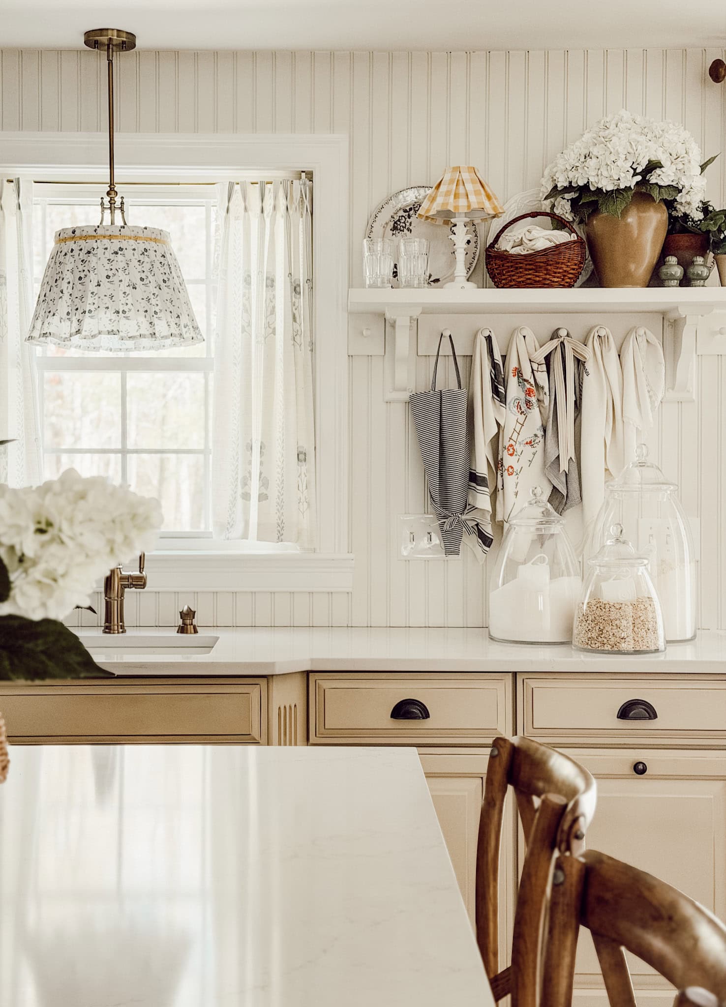 kitchen shelf decorated with cottage decor beside a kitchen sink that is below a window