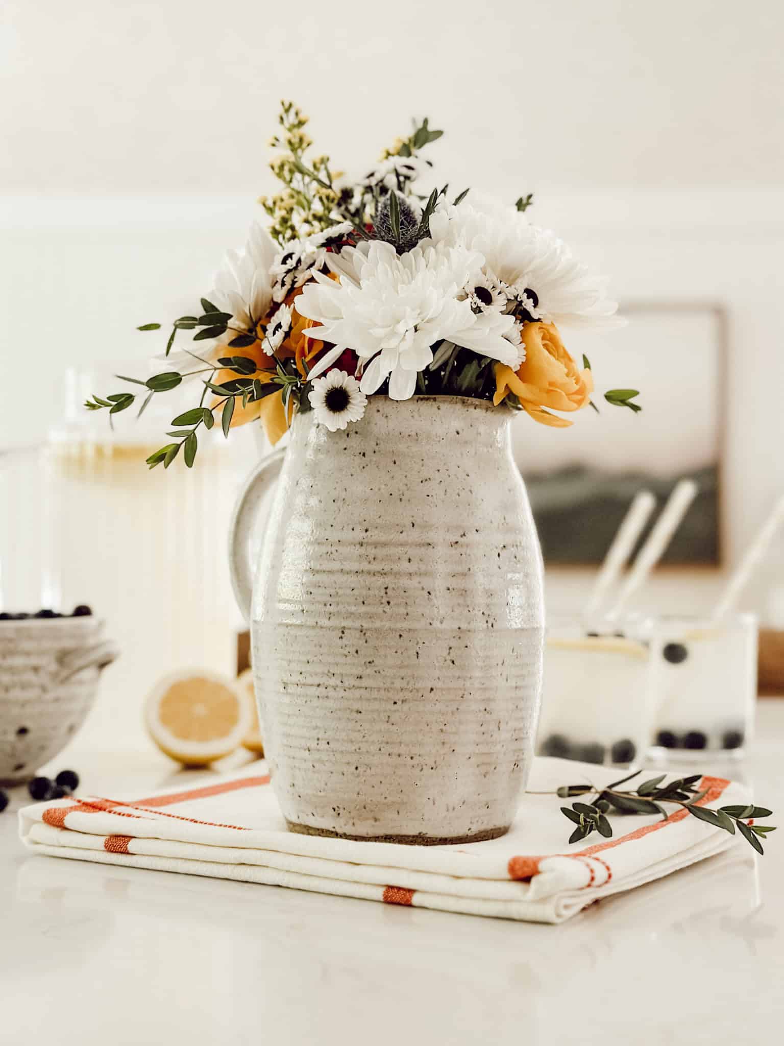 large white stoneware vase filled with white and coral flowers and greenery stems