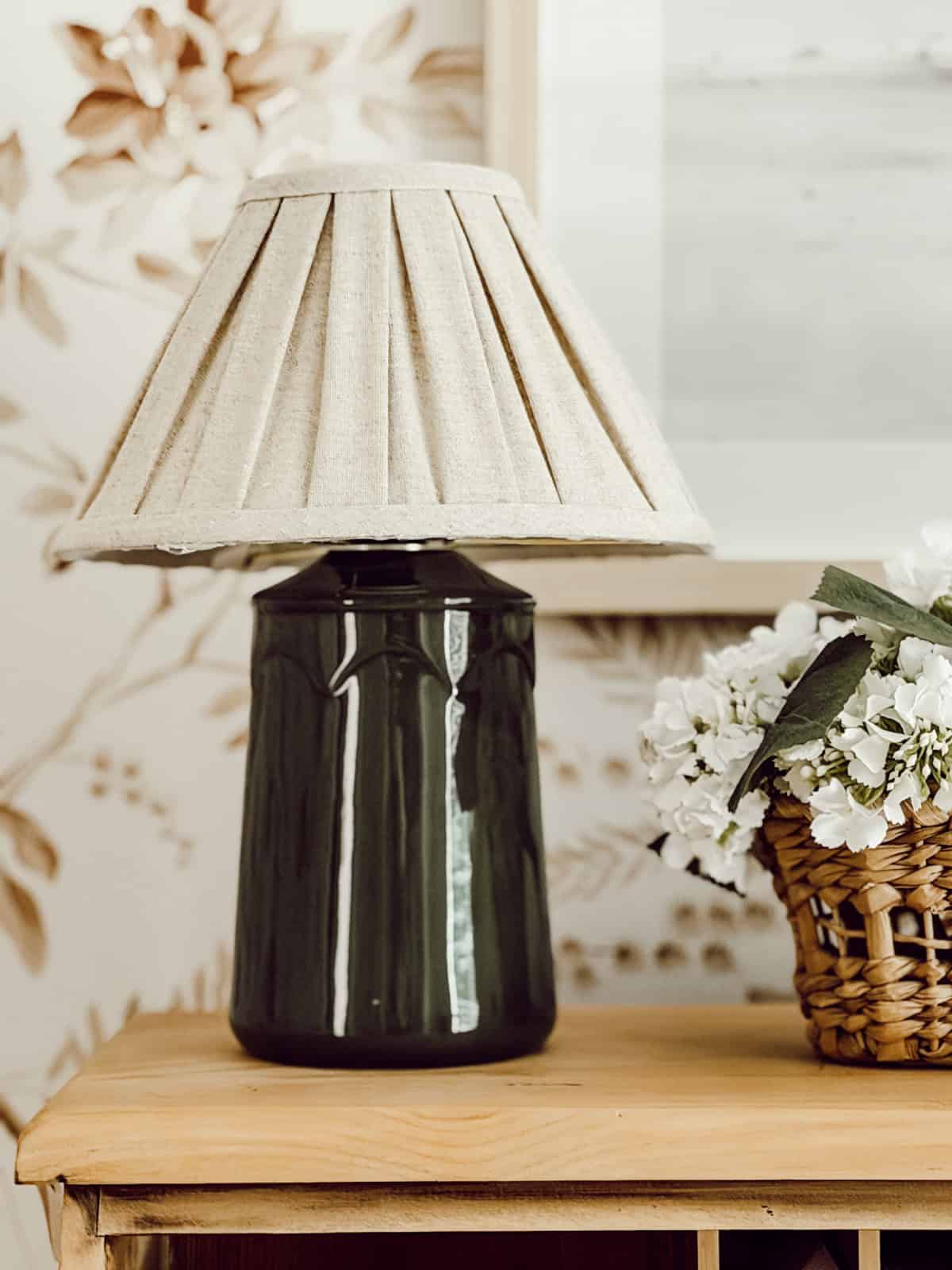 table lamp with a black base and neutral pleated shade sitting on a pine table