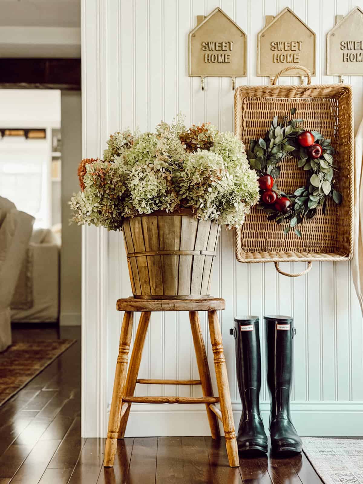 wooden slat basket filled with dried hydrangeas sitting on a wood stool in front of a decorated wall