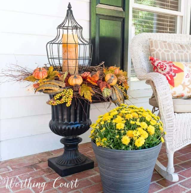 Pumpkin fall centerpiece with candles and autumn leaves on outdoor porch.