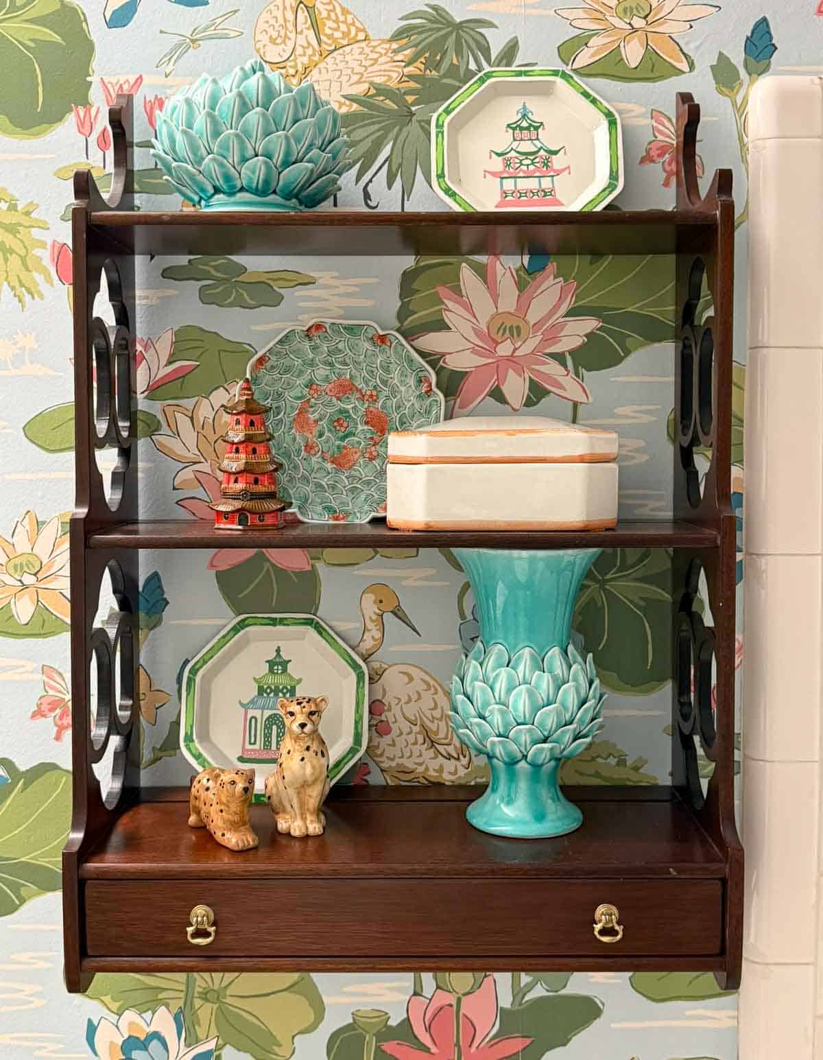small wooden shelves hanging on a wallpapered wall with traditional accessories
