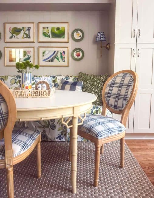Bright breakfast nook with a floral banquette, plaid dining chairs, botanical artwork, and blue, green, and taupe accents.