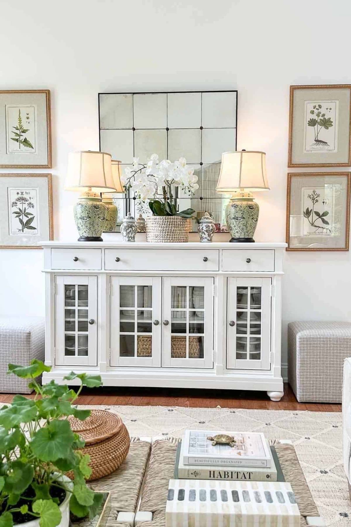 white console with glass doors against a white wall with artwork and a mirror above and neutral lamps and accessories