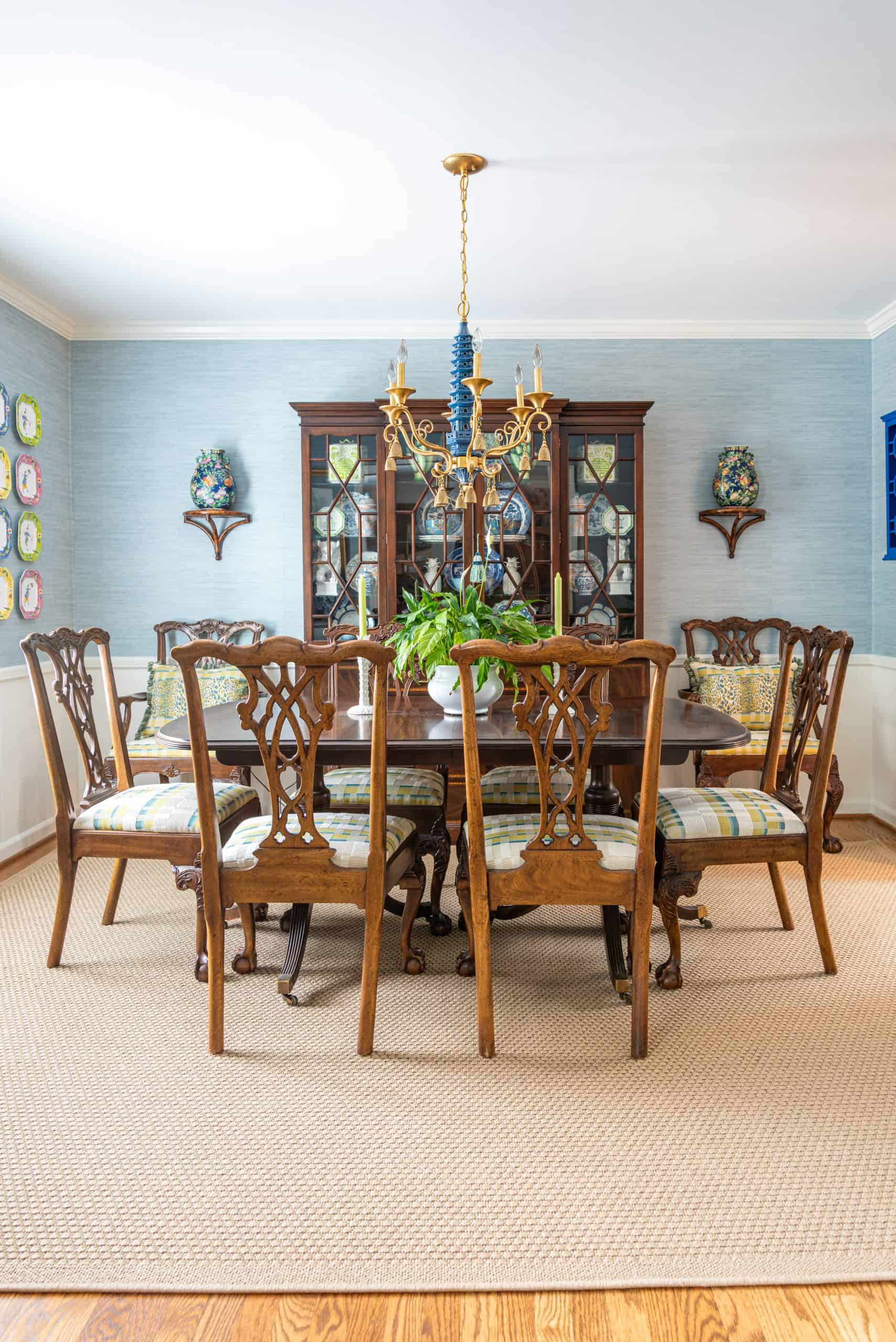 Traditional dining room with blue grasscloth walls, antique wood dining table and chairs, blue and white china, brass chandelier, and colorful chinoiserie accents.