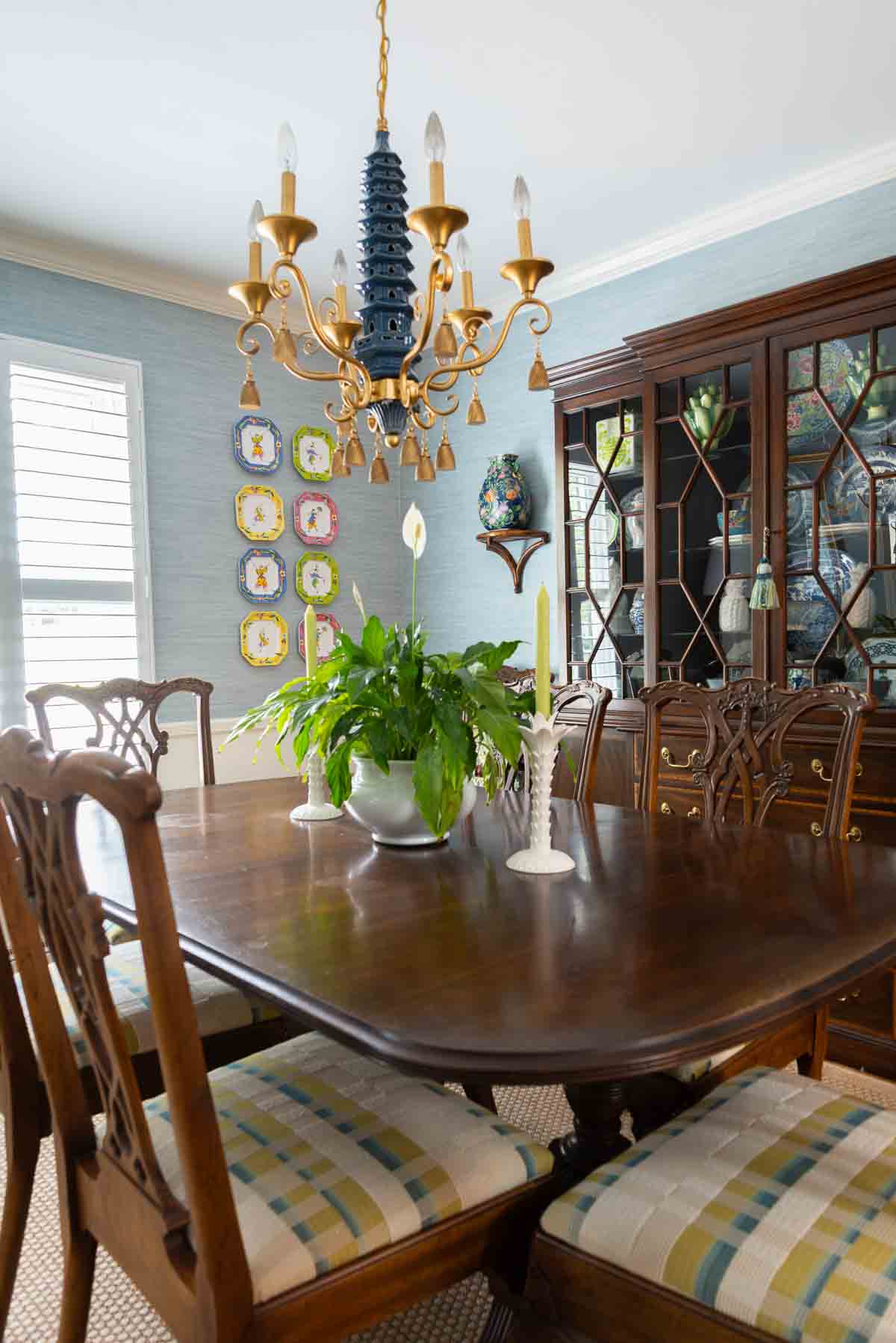 Traditional dining room with blue grasscloth walls, antique wood dining table and chairs, blue and white china, brass chandelier, and colorful chinoiserie accents.