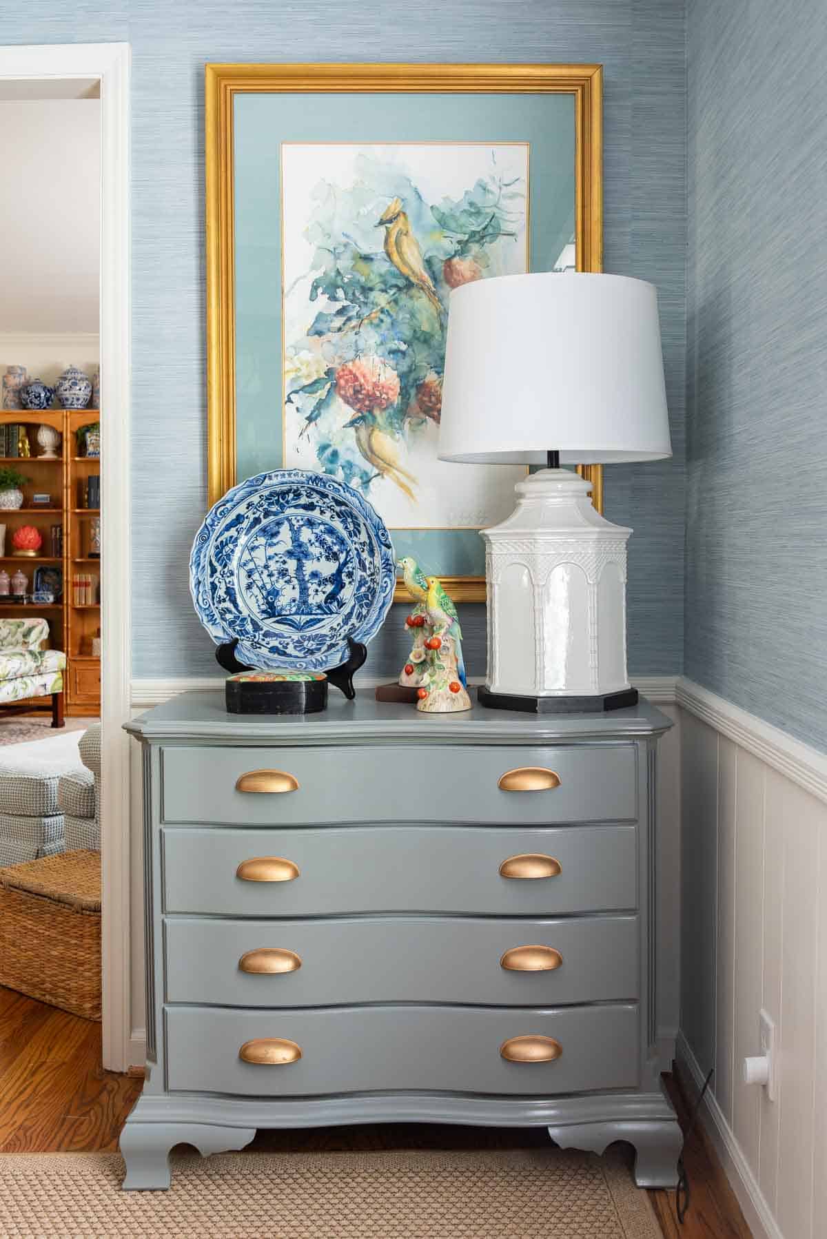 Traditional dining room with blue grasscloth walls, antique wood dining table and chairs, blue and white china, brass chandelier, and colorful chinoiserie accents.
