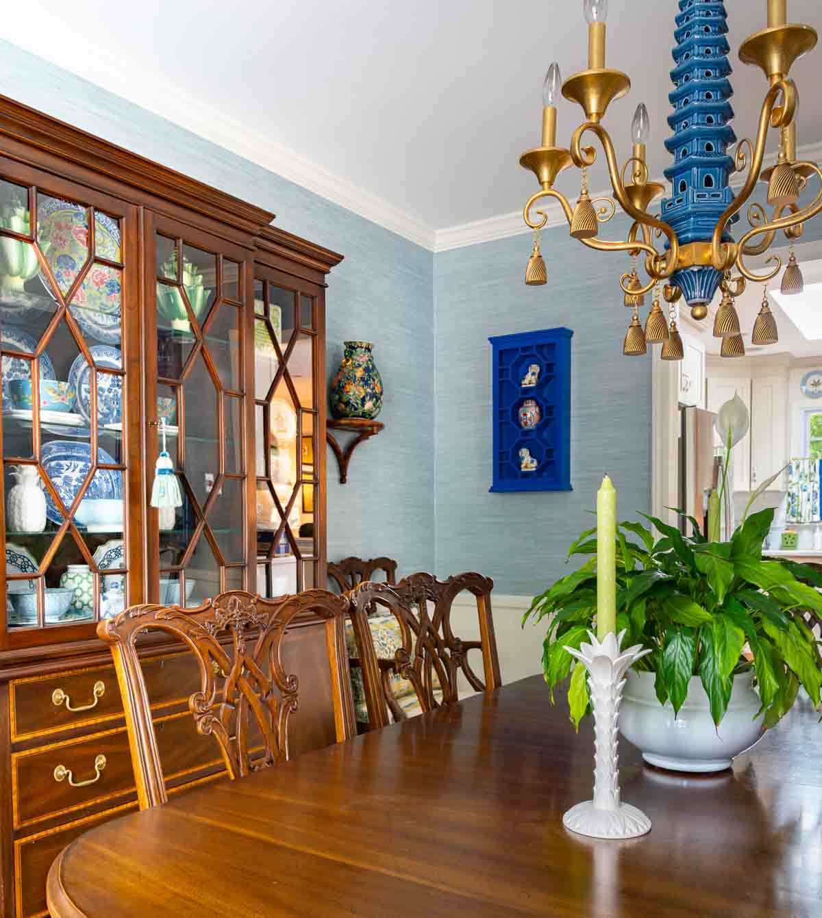 Traditional dining room with blue grasscloth walls, antique wood dining table and chairs, blue and white china, brass chandelier, and colorful chinoiserie accents.