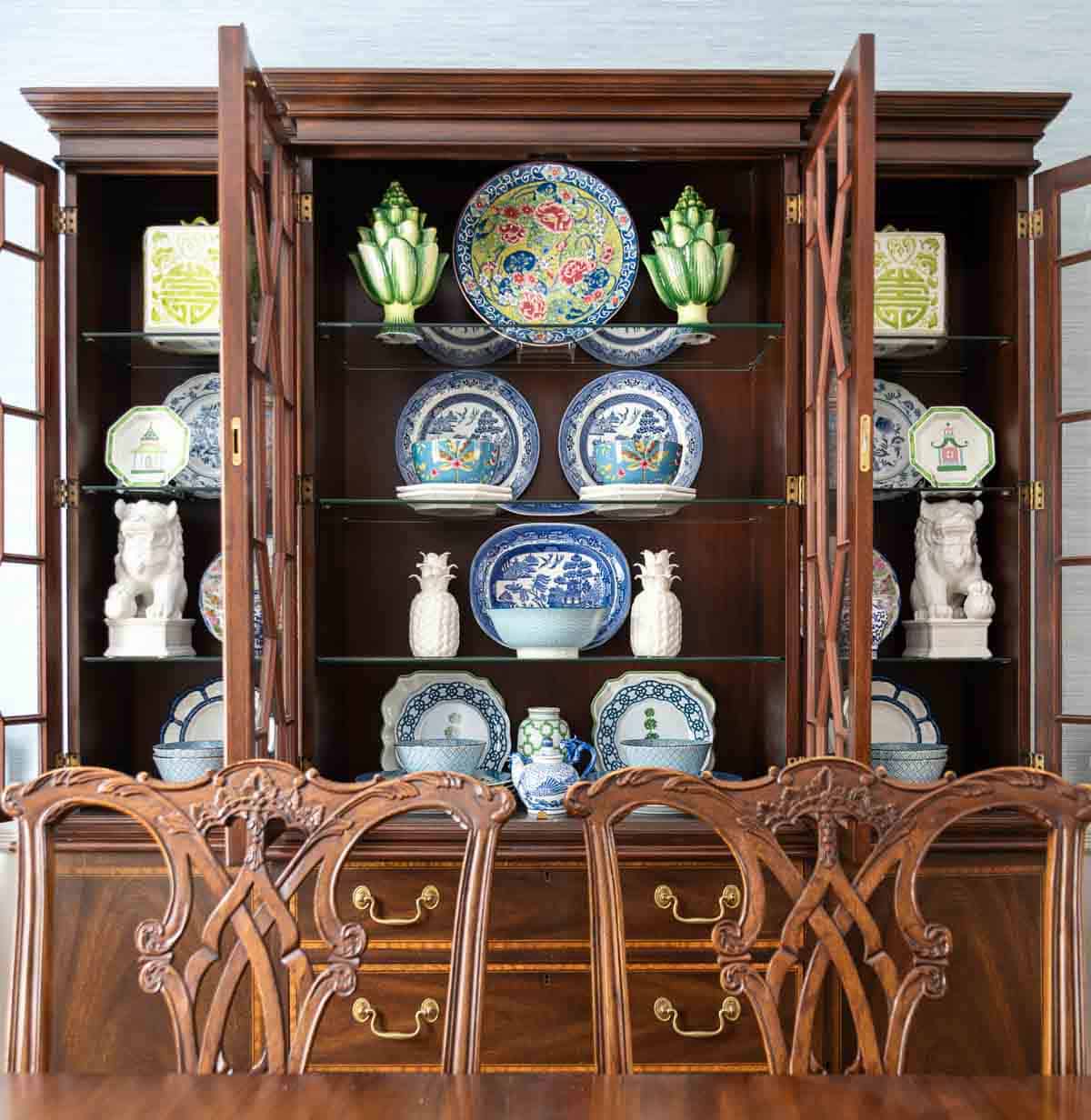 Traditional dining room with blue grasscloth walls, antique wood dining table and chairs, blue and white china, brass chandelier, and colorful chinoiserie accents.