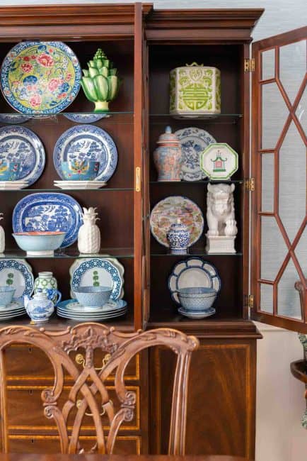 Traditional dining room with blue grasscloth walls, antique wood dining table and chairs, blue and white china, brass chandelier, and colorful chinoiserie accents.