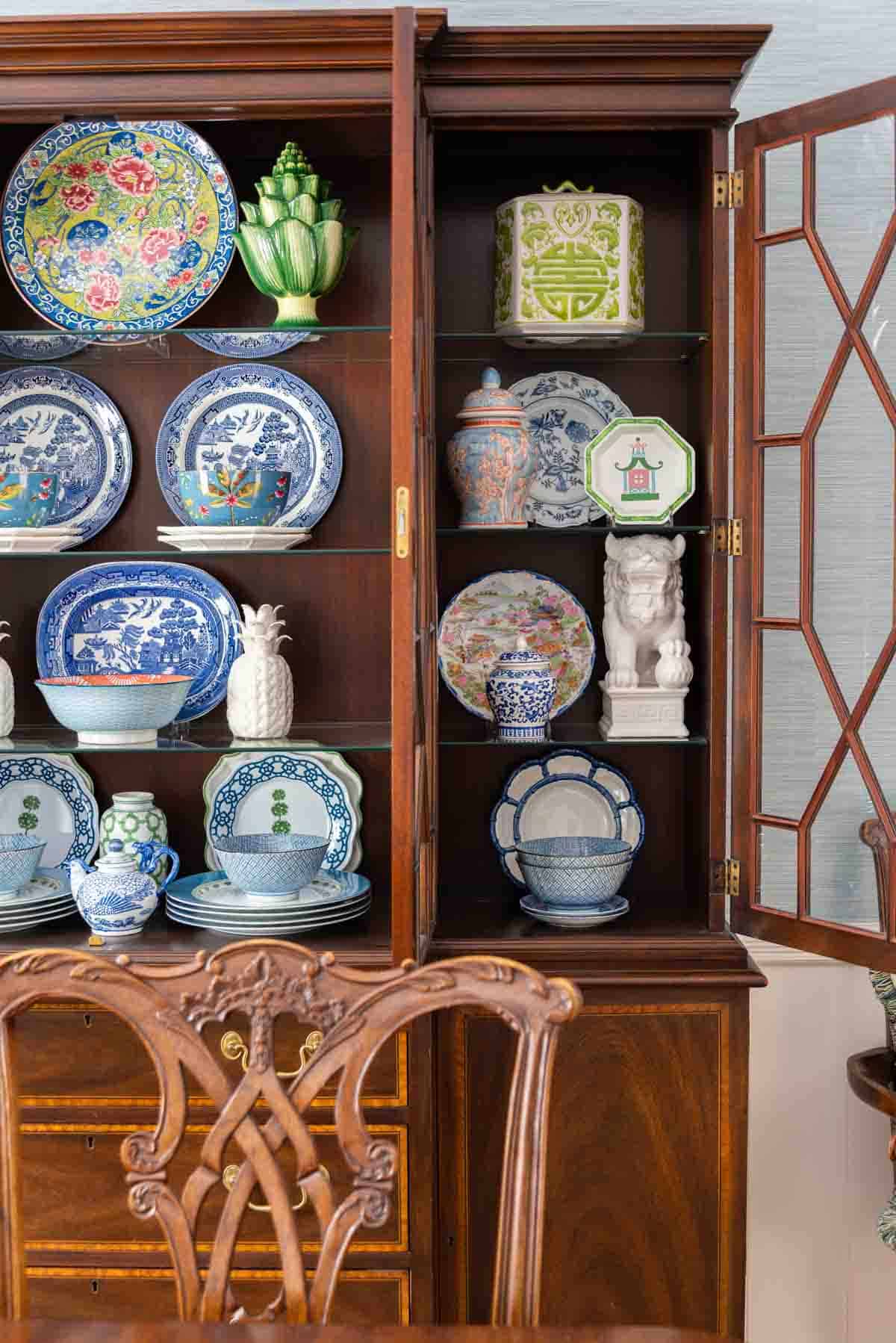 Traditional dining room with blue grasscloth walls, antique wood dining table and chairs, blue and white china, brass chandelier, and colorful chinoiserie accents.