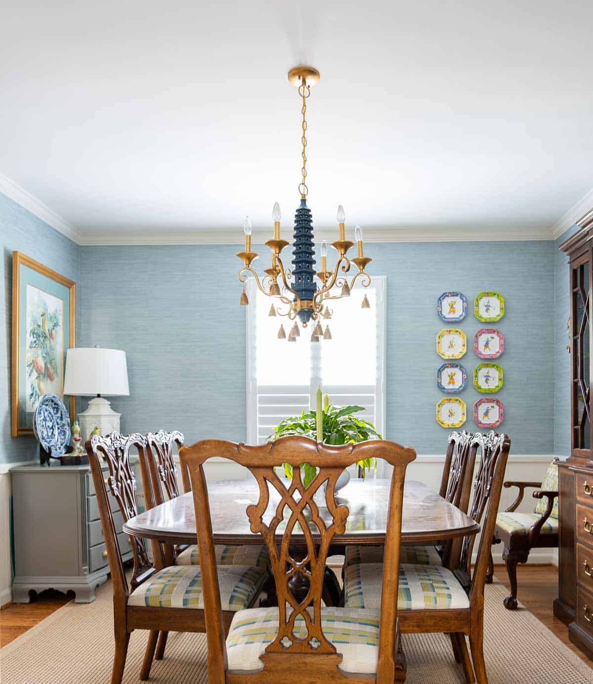 Traditional dining room with blue grasscloth walls, antique wood dining table and chairs, blue and white china, brass chandelier, and colorful chinoiserie accents.