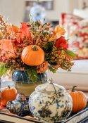 vase filled with fall foliage in a tray with blue and white accessories on a coffee table