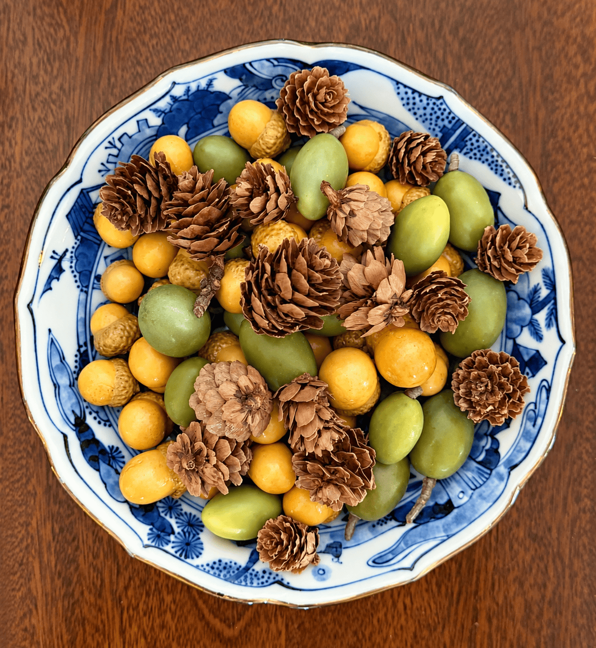 blue and white chinoiserie bowl filled with acorns and tiny pinecones on a wood table